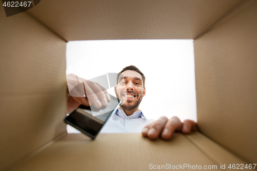 Image of smiling man taking smartphone out parcel box