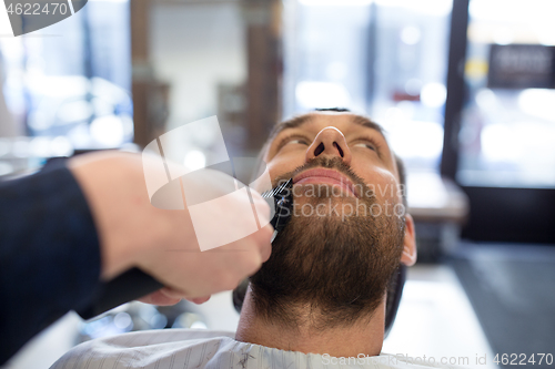 Image of man and barber with trimmer cutting beard at salon