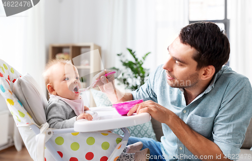 Image of father feeding happy baby in highchair at home