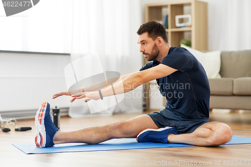 Image of man stretching leg on exercise mat at home