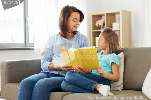 Image of happy girl with mother reading book at home