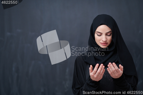 Image of muslim woman making traditional prayer to God in front of black 