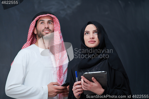 Image of muslim couple using modern technology in front of black chalkboa