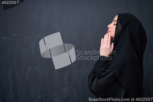 Image of muslim woman making traditional prayer to God in front of black 