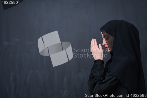 Image of muslim woman making traditional prayer to God in front of black 