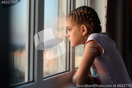 Image of Eleven-year-old girl in isolation from boredom looks out the window