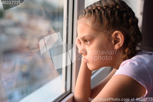 Image of Tired of self-isolation, a bored quarantine girl looks out the window