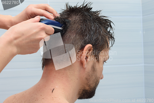 Image of Girl cuts hair with a clipper on a man\'s head at home in the bathroom