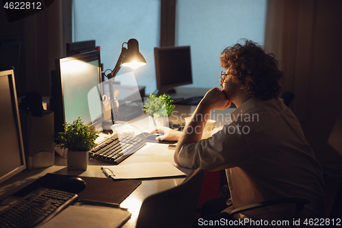 Image of Man working in office alone during coronavirus or COVID-19 quarantine, staying to late night