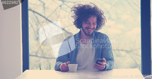 Image of young man drinking coffee and using a mobile phone  at home