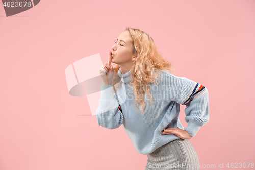 Image of The young woman whispering a secret behind her hand over pink background