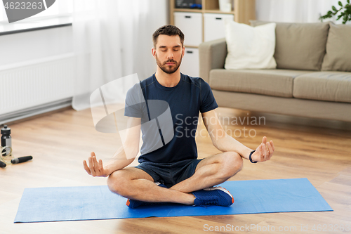 Image of man meditating in lotus pose on yoga mat at home