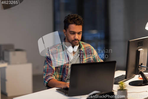 Image of creative man with laptop working at night office