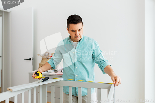 Image of father with tablet pc and ruler measuring baby bed