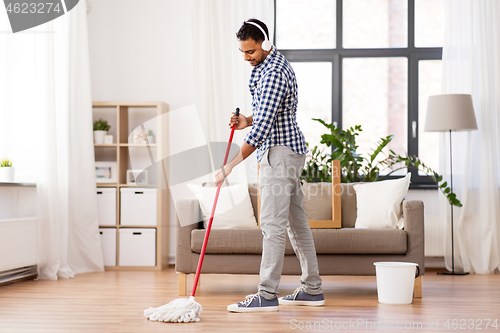 Image of man in headphones with mop cleaning floor at home