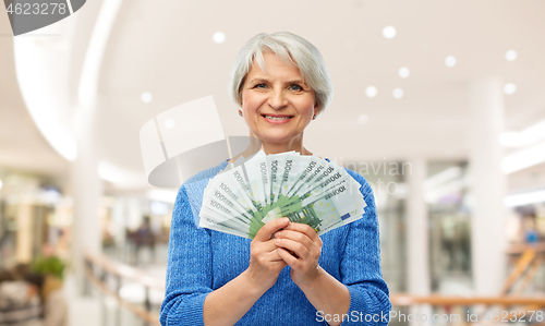 Image of senior woman with euro money over shopping mall