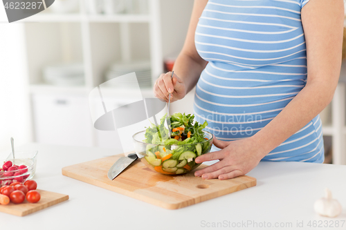 Image of close up of pregnant woman cooking salad at home