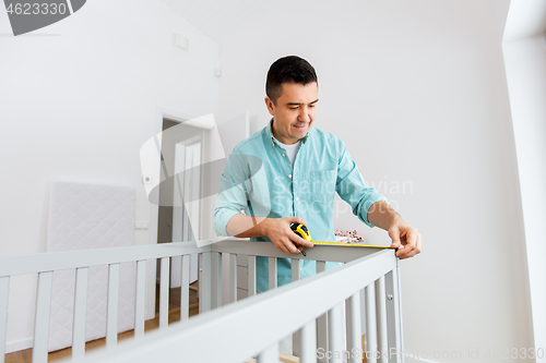 Image of father with tablet pc and ruler measuring baby bed