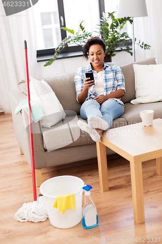 Image of woman with smartphone resting after home cleaning