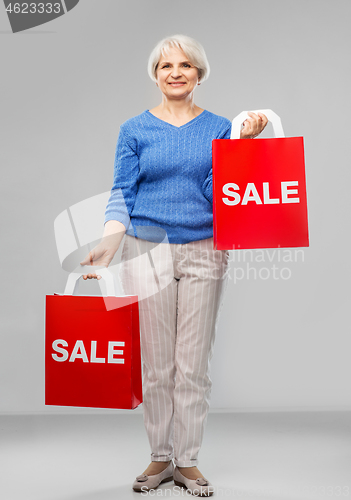 Image of senior woman with sale word on red shopping bags