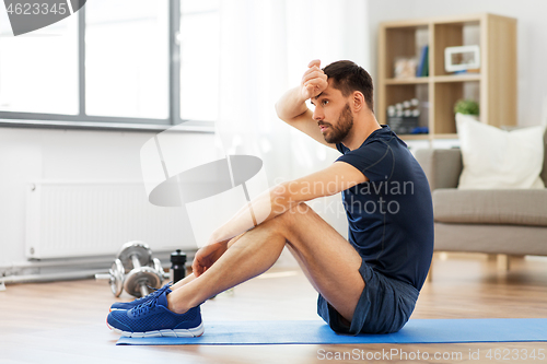 Image of tired man sitting on exercise mat at home