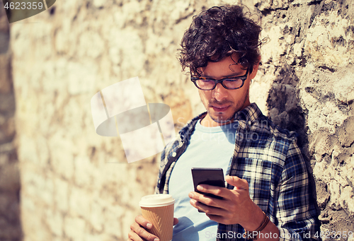 Image of man with smartphone drinking coffee on city street