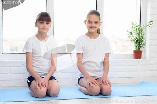 Image of Two sisters are sitting at home on a sports mat before training