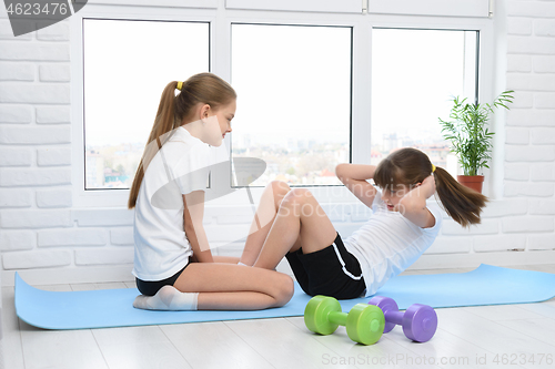 Image of Older sister helps younger to do exercise for the press