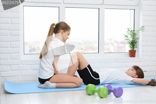 Image of Two girls perform sports exercises at home during self-isolation