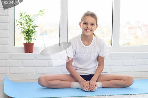 Image of Teen girl sitting on a sports mat before training at home