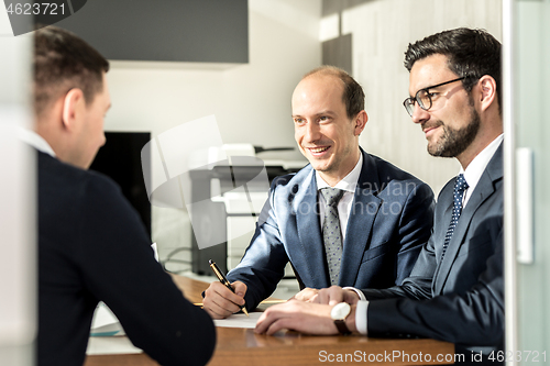 Image of Group of confident successful business people reviewing and signing a contract to seal the deal at business meeting in modern corporate office.