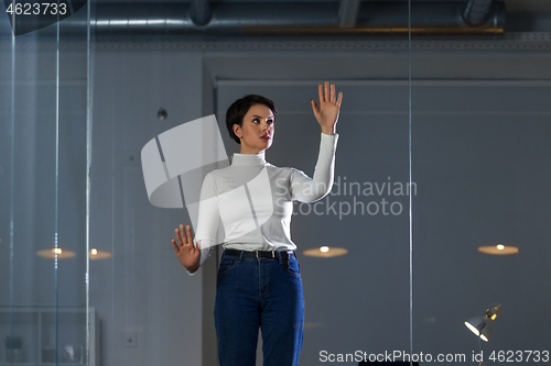 Image of businesswoman using glass wall at night office