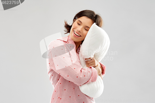 Image of happy young woman in pajama hugging pillow