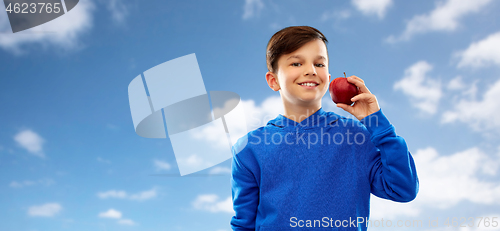 Image of smiling boy in hoodie with red apple over blue sky