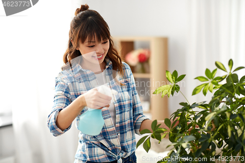 Image of happy asian woman spraying houseplant at home