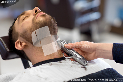 Image of man and barber with trimmer cutting beard at salon