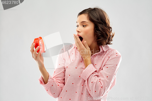 Image of shocked young woman in pajama with alarm clock