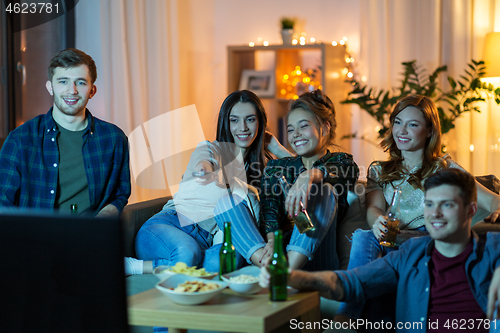 Image of friends with drinks and snacks watching tv at home