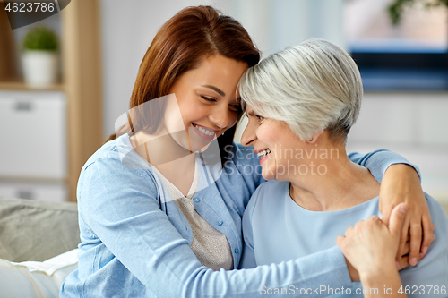 Image of senior mother with adult daughter hugging at home