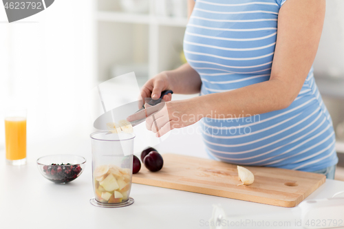 Image of pregnant woman chopping fruits at home kitchen