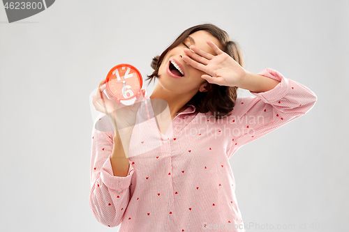 Image of sleepy young woman in pajama with alarm clock