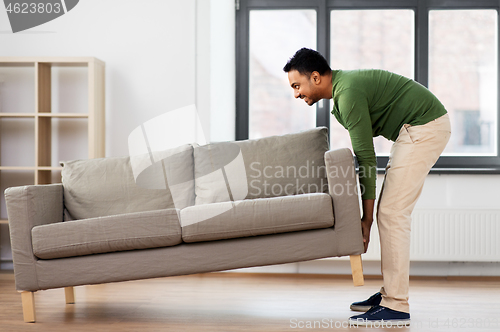 Image of happy indian man moving sofa at home