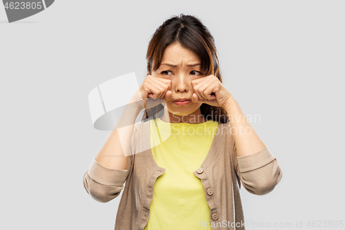 Image of sad asian woman crying over grey background