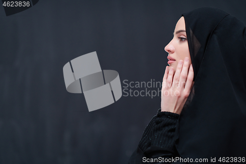 Image of muslim woman making traditional prayer to God in front of black 