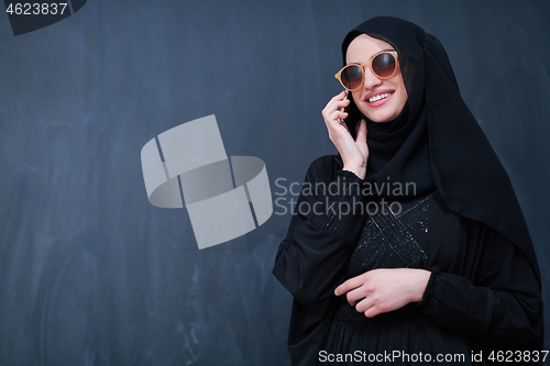 Image of young muslim woman wearing sunglasses using smartphone