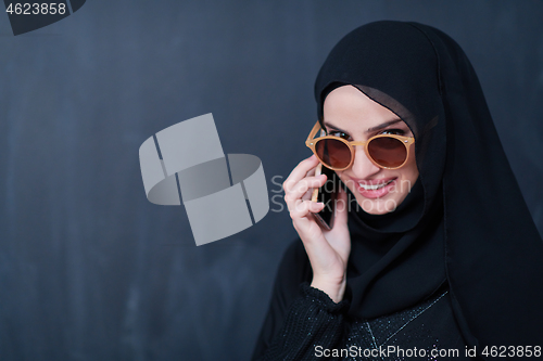 Image of young muslim woman wearing sunglasses using smartphone