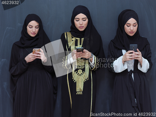 Image of muslim women using mobile phone in front of black chalkboard