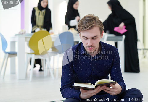 Image of young muslim man reading Quran at home