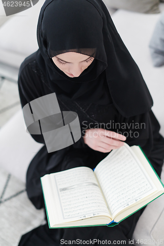 Image of young muslim woman reading Quran at home