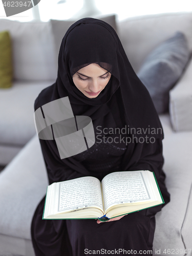 Image of young muslim woman reading Quran at home